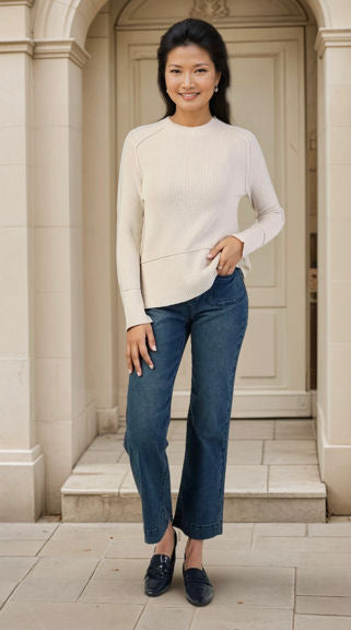 Woman wearing a white sweater and blue jeans standing in front of a stone building.