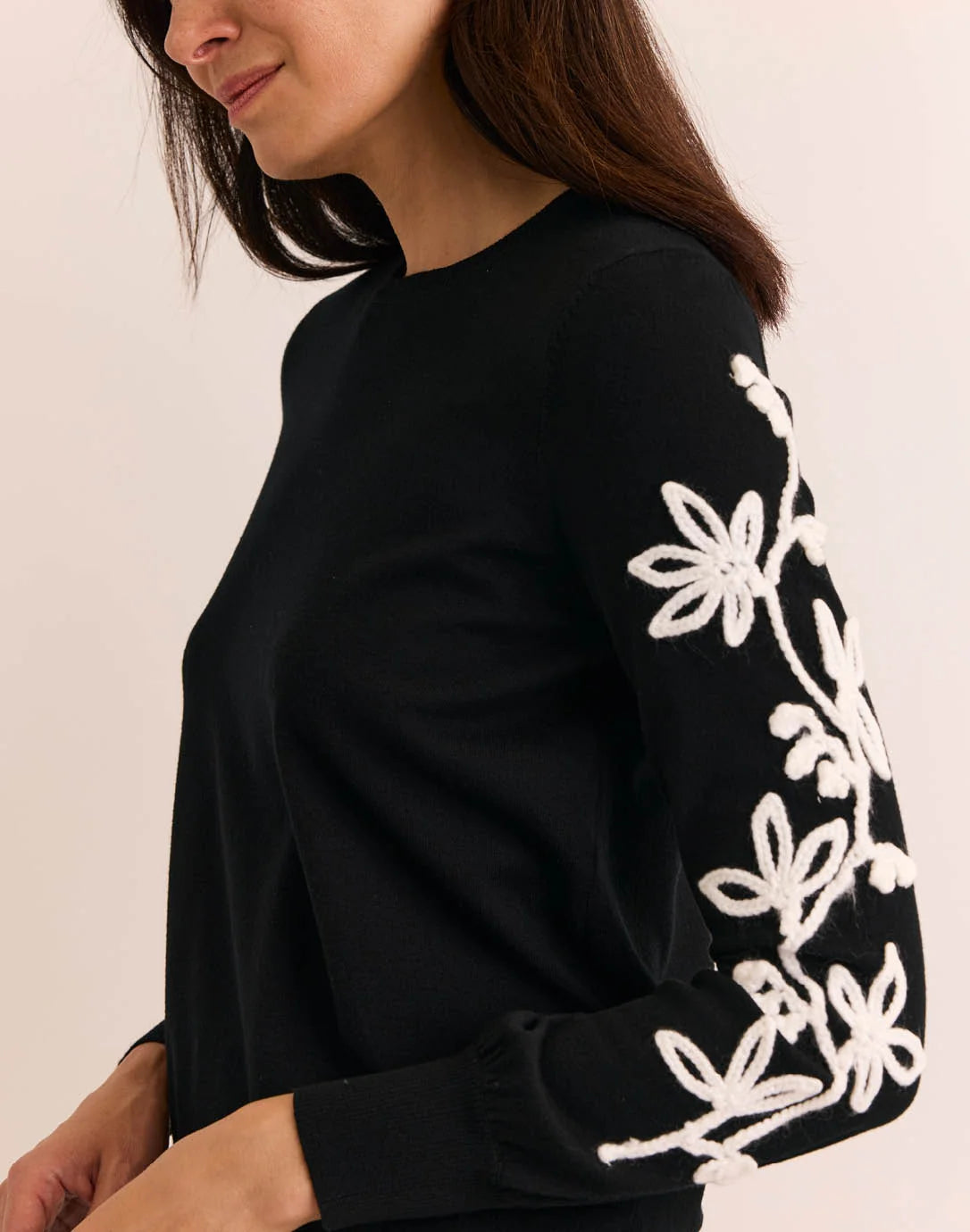 Woman wearing a black sweater with white floral patterns, The H Edition Kannon Long Sleeve Embroidered Sweater