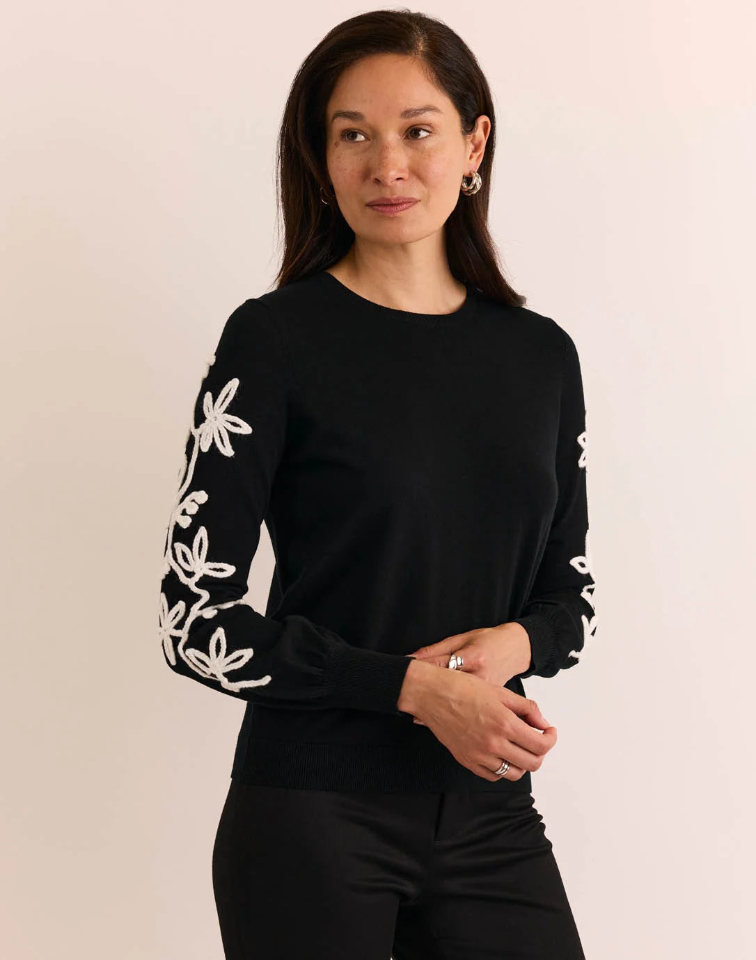 Woman wearing a black sweater with white floral patterns, The H Edition Kannon Long Sleeve Embroidered Sweater