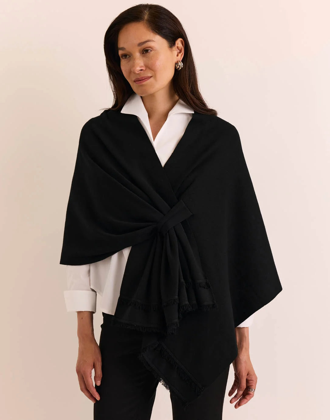 A woman modeling a black wrap shawl by The H Edition Mabel Tab Fringe Wrap