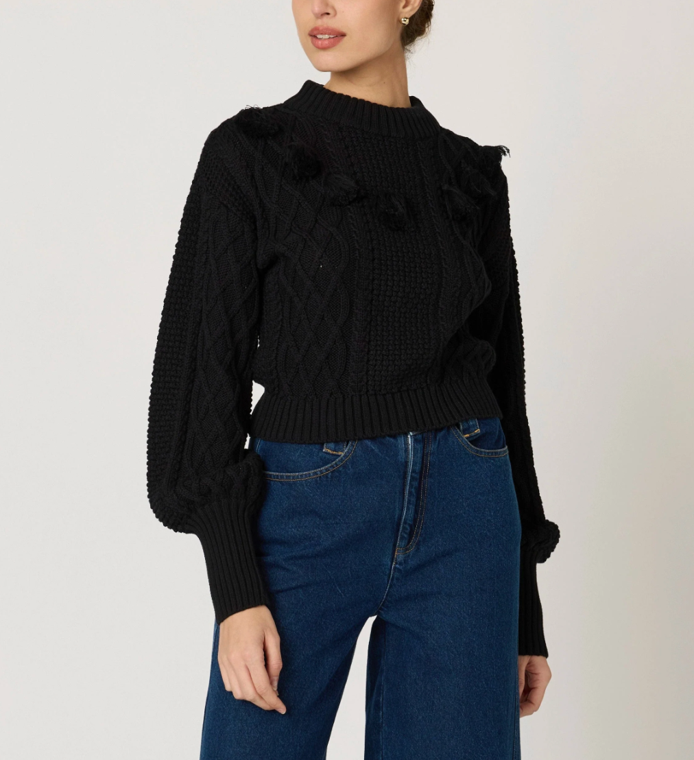 woman wearing a black knit sweater, textured with tassel details around the top