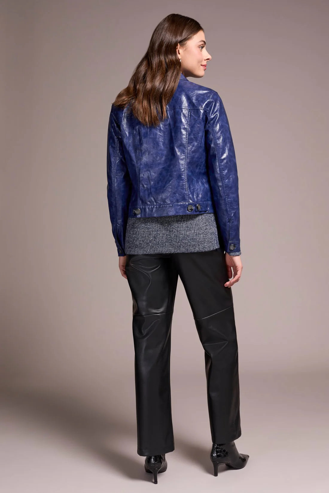 Woman wearing a blue leather jacket and black pants on a beige background