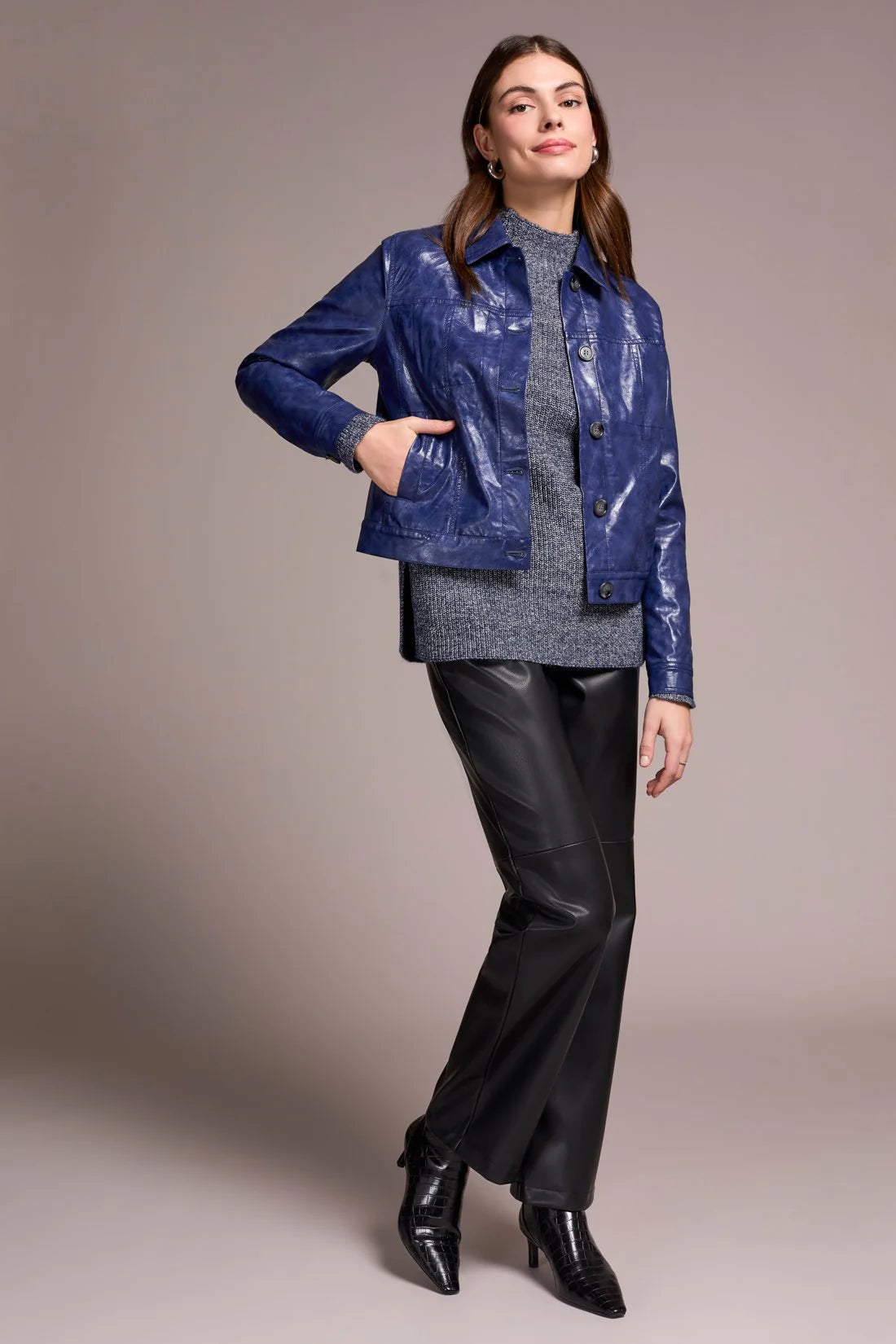 Woman wearing a blue jacket, gray sweater, and black pants against a plain background