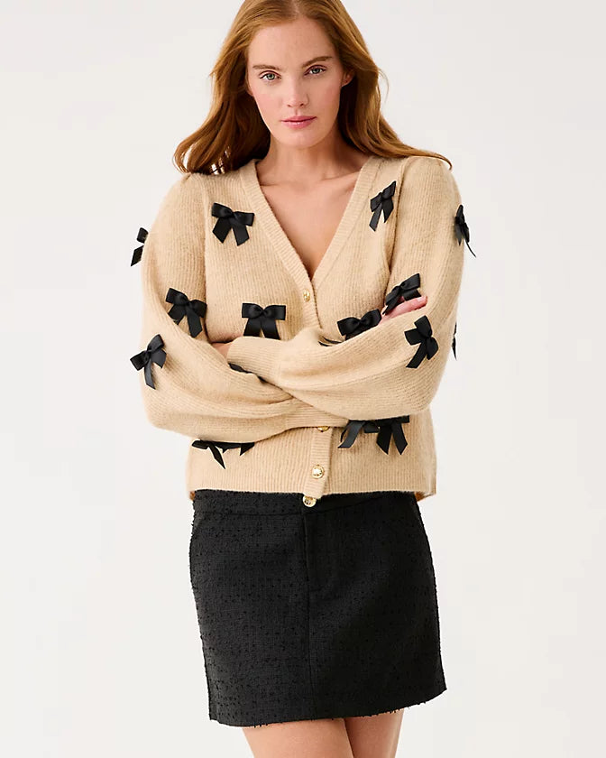 Woman wearing a beige cardigan with black bow details on a white background