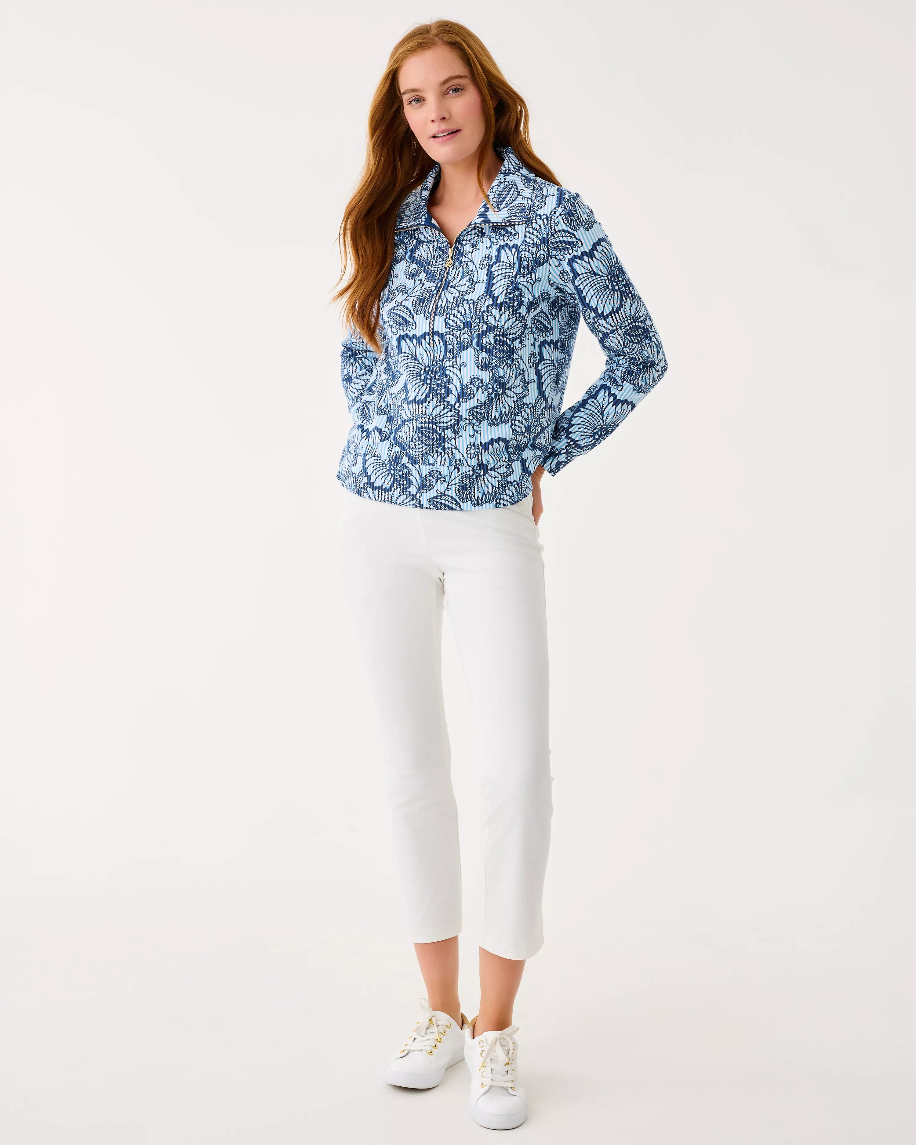 Woman wearing a blue patterned blouse and white pants on a white background