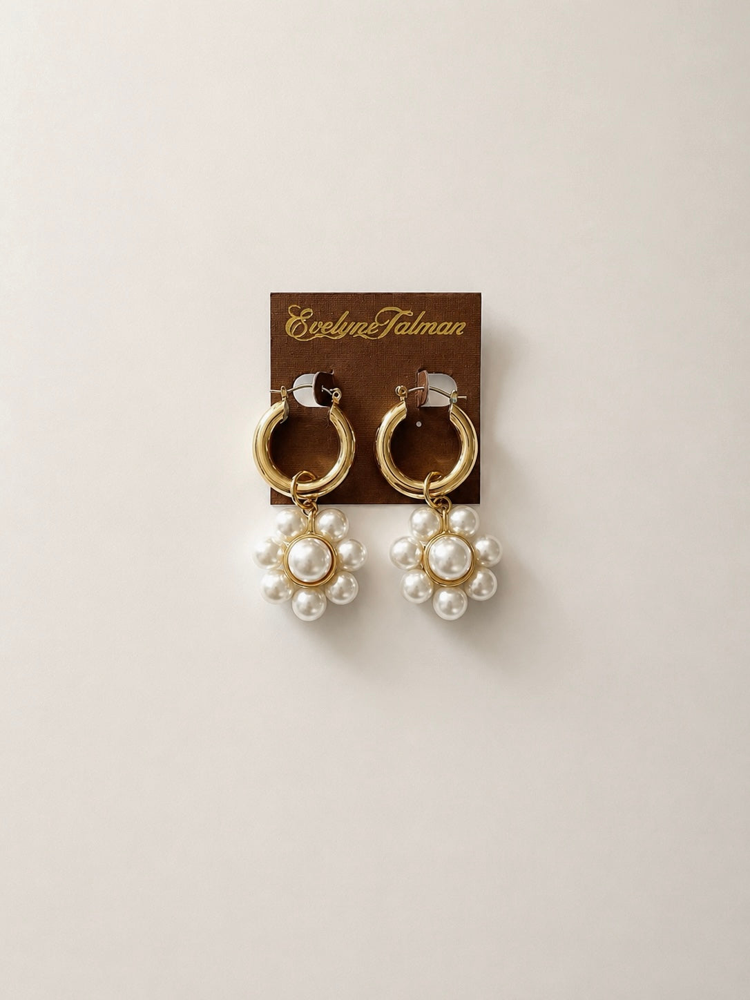 A pair of gold hoop earrings with dangling clusters of white faux pearls in a flower shape