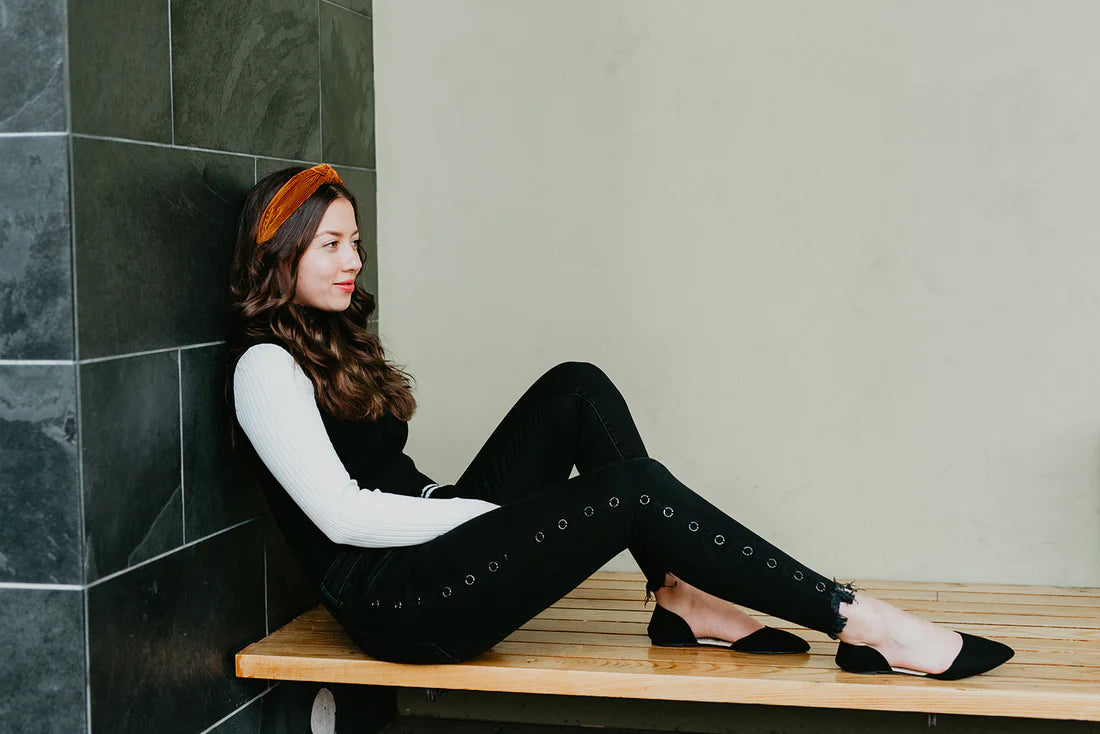 Woman sitting on a wooden bench against a tiled wall.