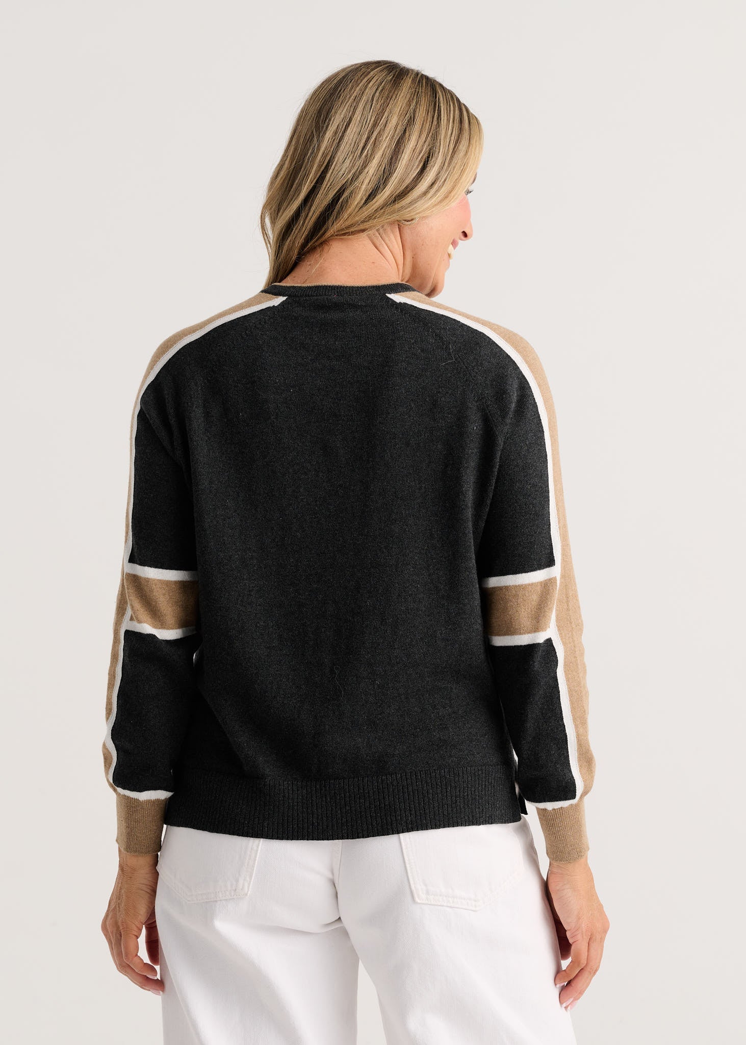 A woman viewed from the back wearing a black knit sweater with beige and white color-blocked shoulder and sleeve stripes Zaket & Plover Block Play Sweater