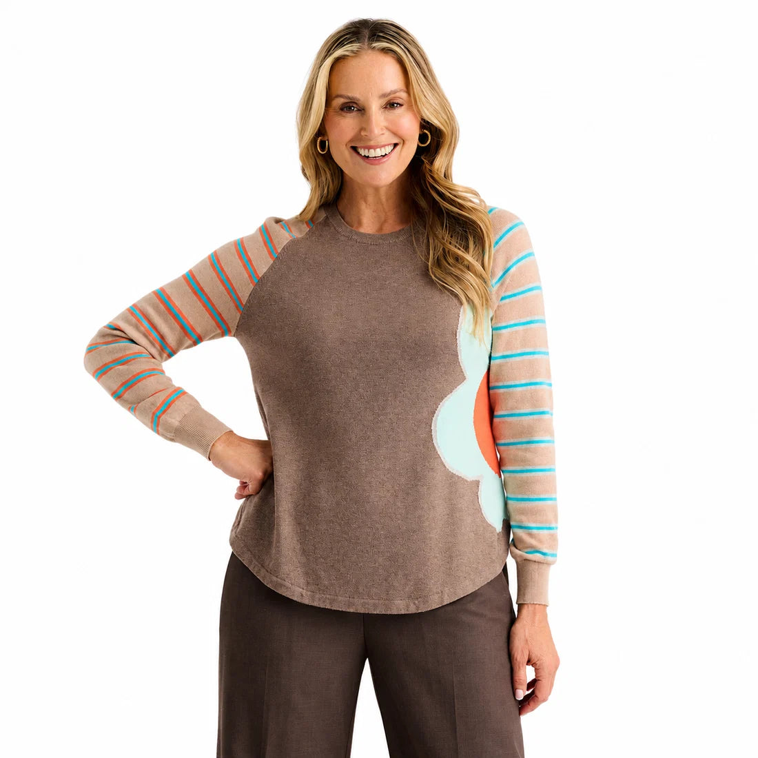 A woman modeling a long-sleeve crewneck top with a solid brown body, peach and turquoise striped sleeves, and a large light blue and coral abstract flower on the right side Zaket & Plover Walnut Bright Side Sweater