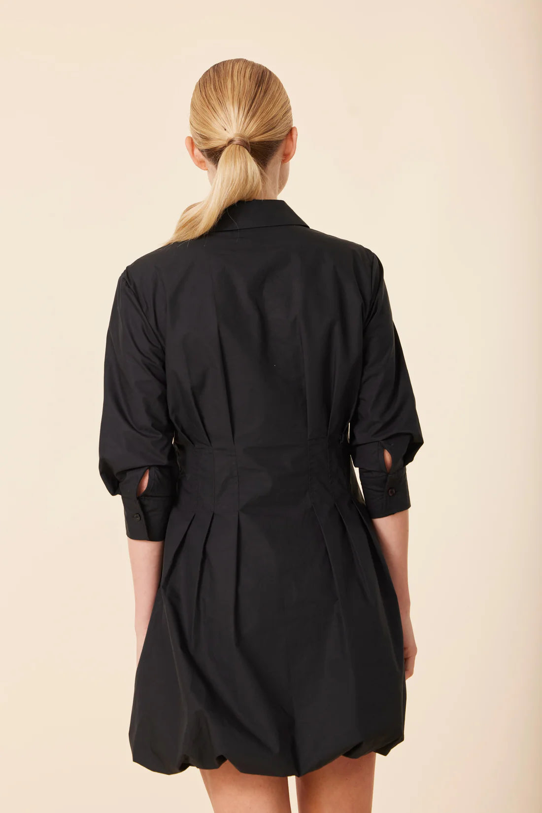 Person wearing a black dress with a belt on a beige background