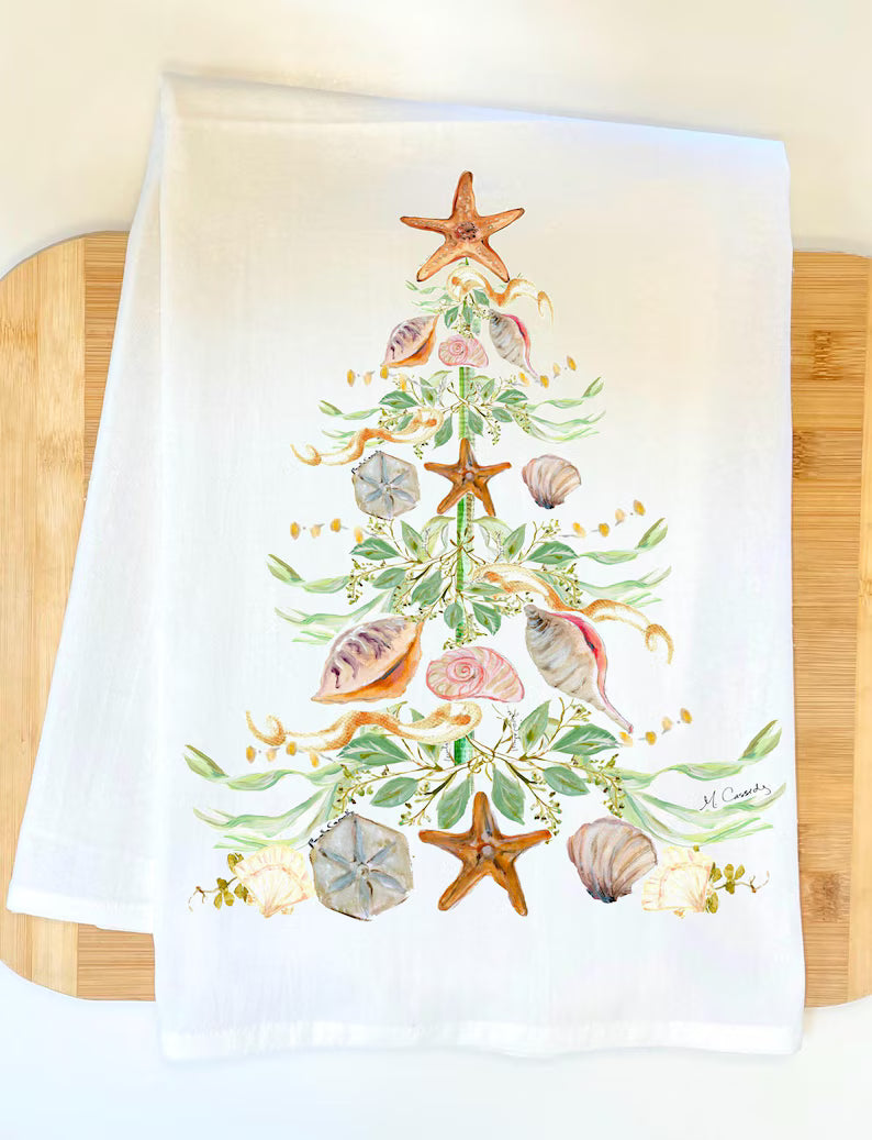White towel with a decorative Christmas tree design featuring shells and starfish on a wooden surface.
