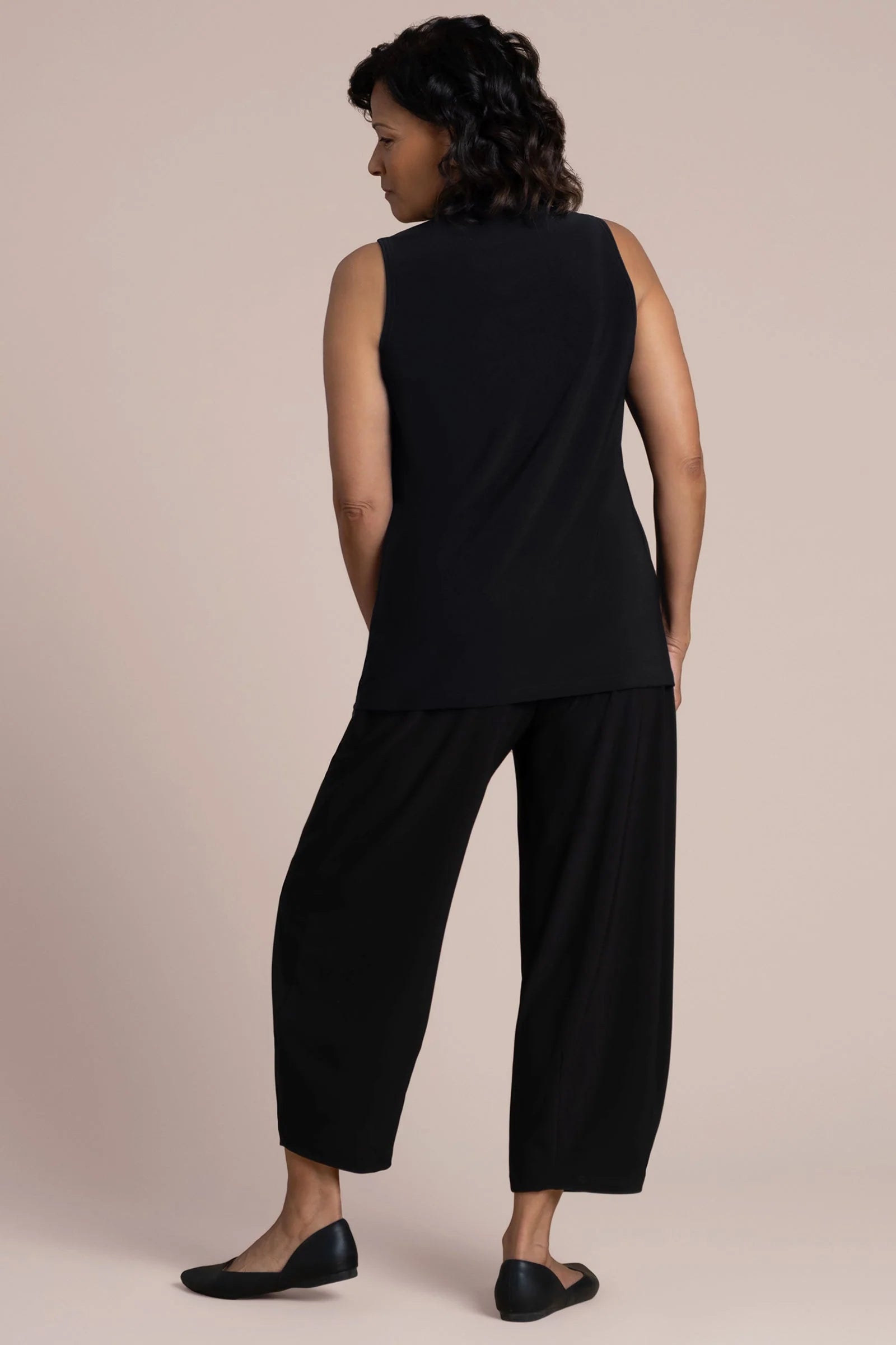 A woman wearing a sleeveless black V-neck top and black pants by Sympli Deep V Trapeze Tank