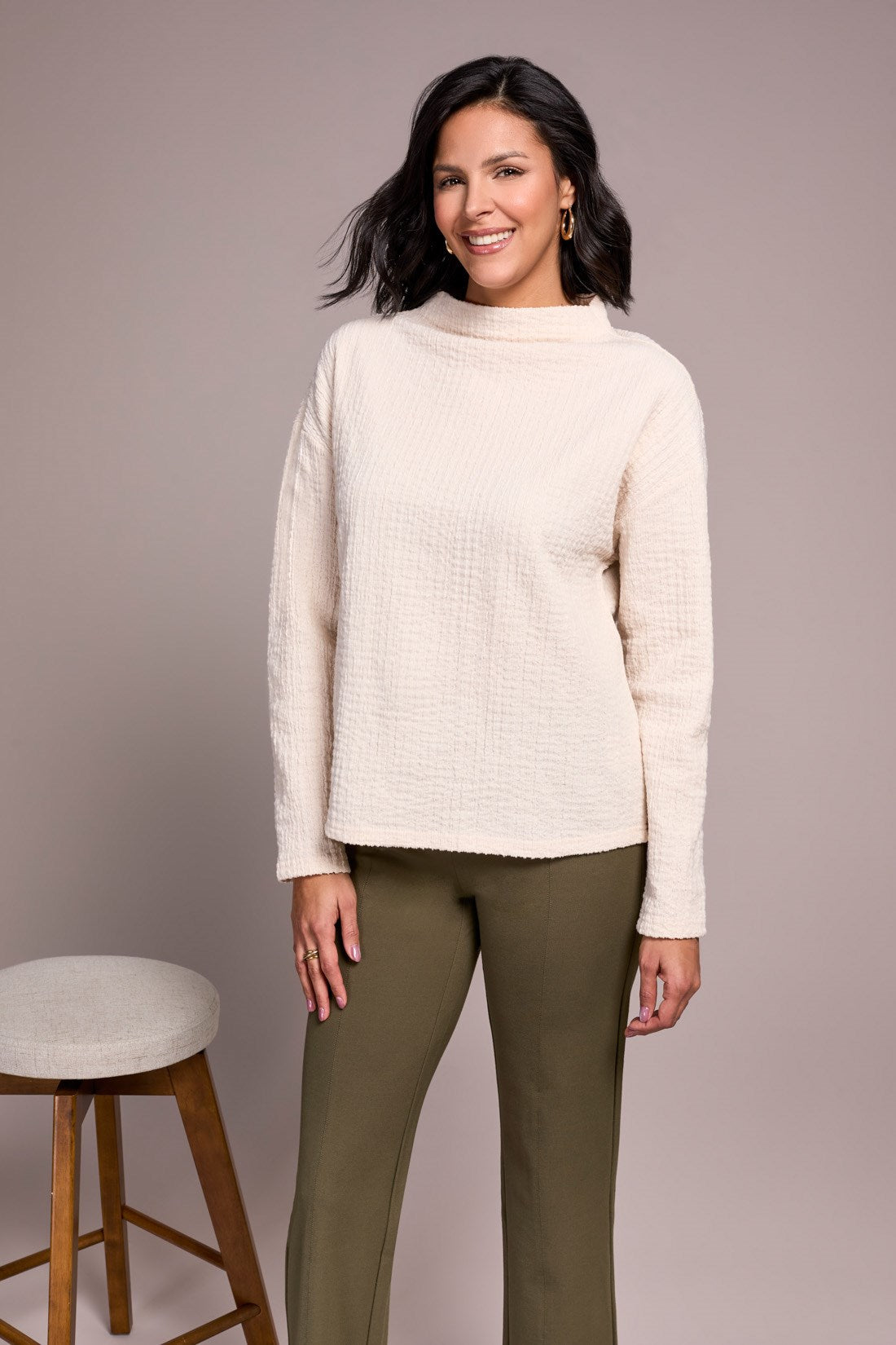 Woman wearing a cream sweater and green pants against a plain background