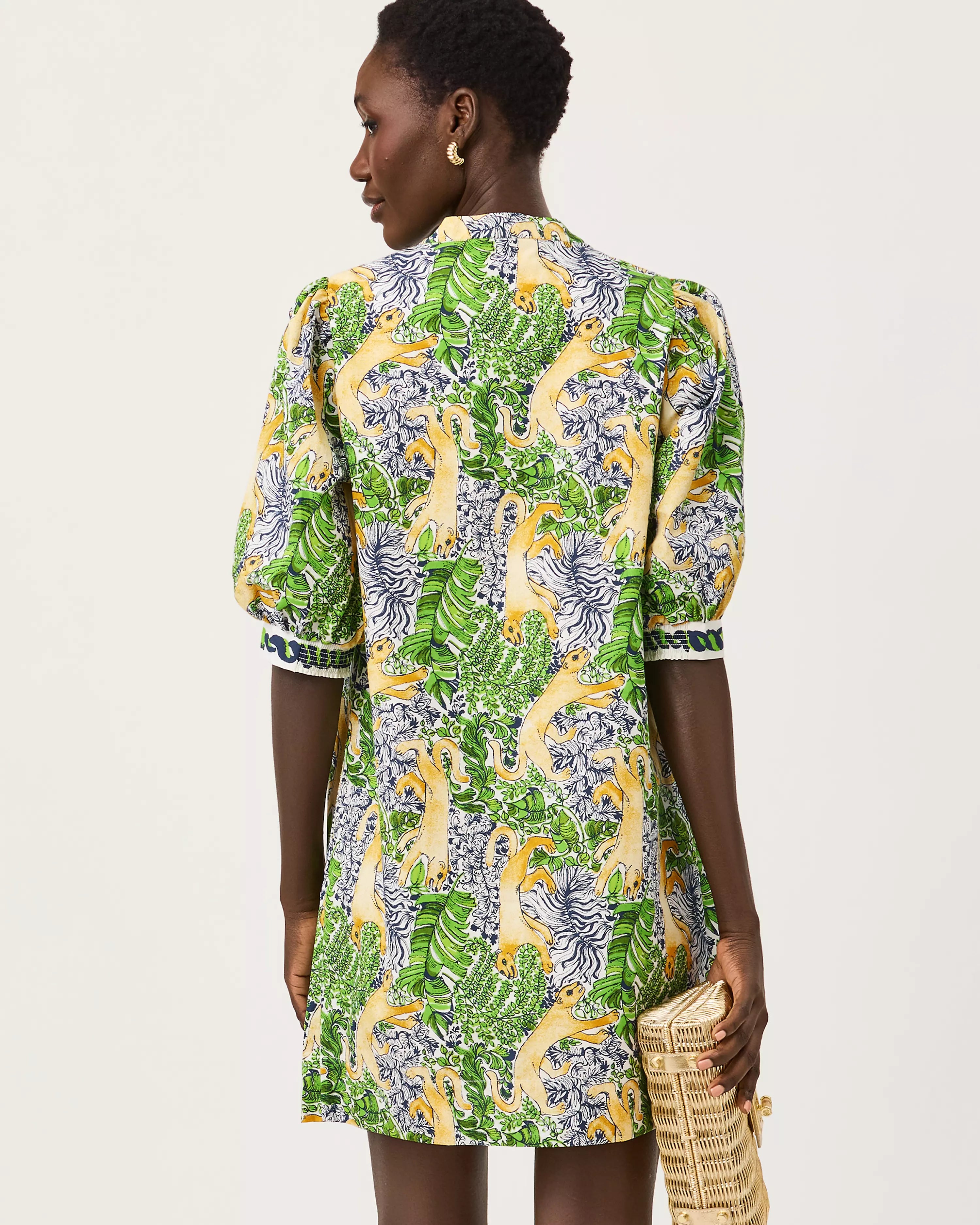 A woman modeling a short-sleeved mini dress with a vibrant green, yellow, and blue floral print lilly pulitzer mialeigh dress Color: Multi Lil Palm Prowl Engineered Woven Dress