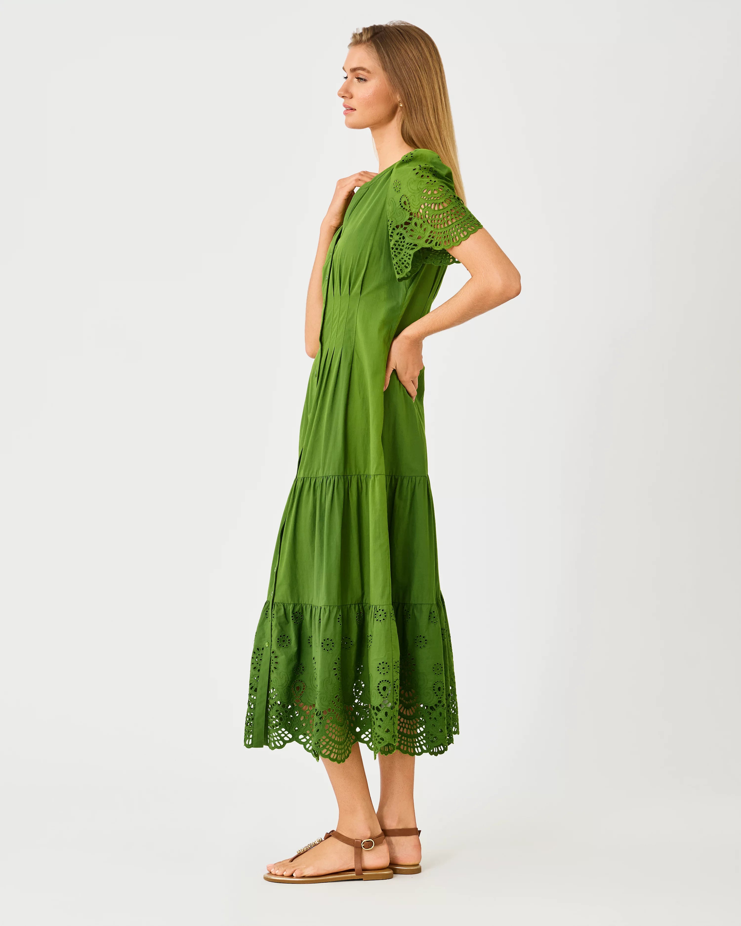 A woman modeling a green midi dress with short puff sleeves, a button-front neckline, and eyelet lace trim at the hem and sleeve cuffs lilly pulitzer wayland midi dress color Oregano Scalloped Eyelet Border Poplin