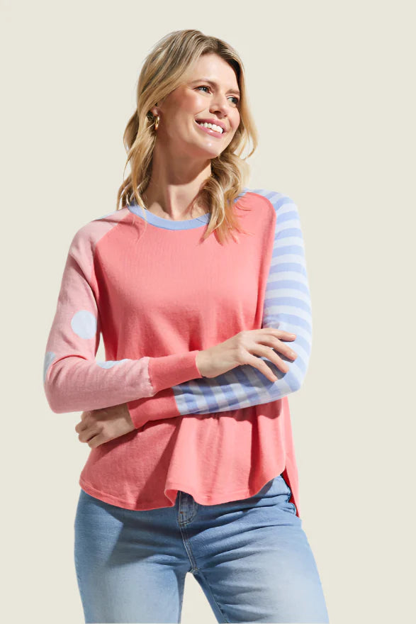 Woman wearing a pink and blue striped long-sleeve top with light blue jeans on a beige background