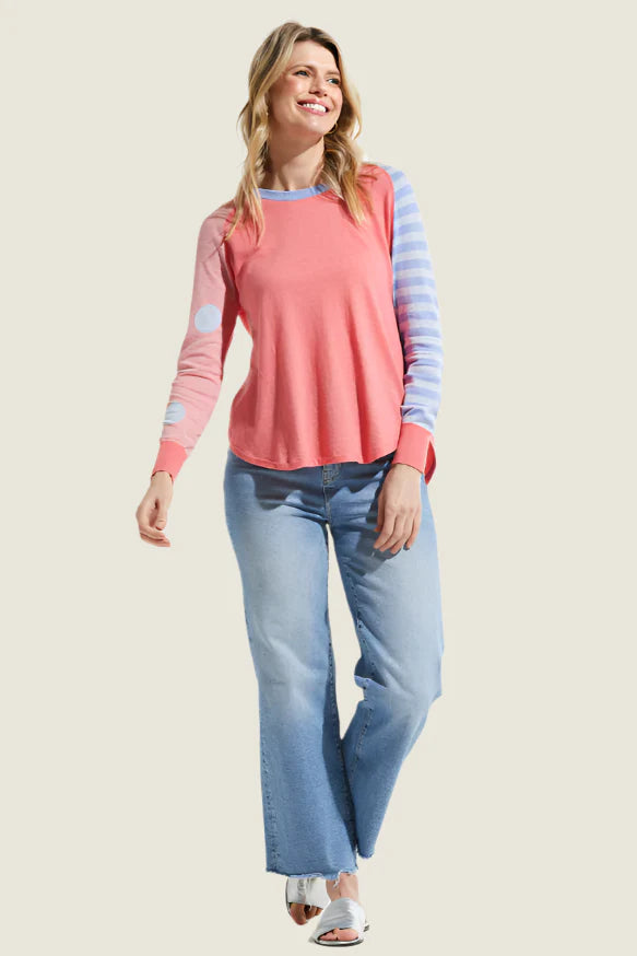 Woman wearing a pink and blue striped long-sleeve top with light blue jeans on a beige background
