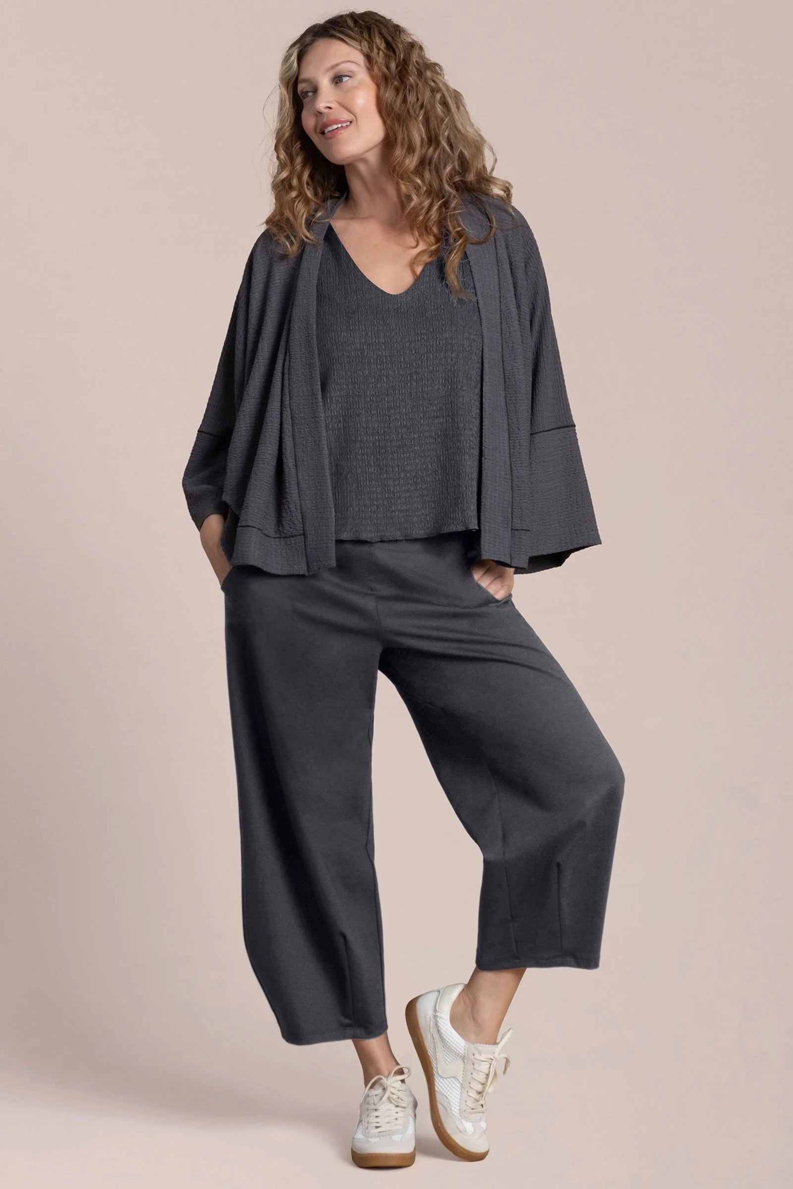 Woman wearing a dark gray outfit with a matching jacket on a beige background