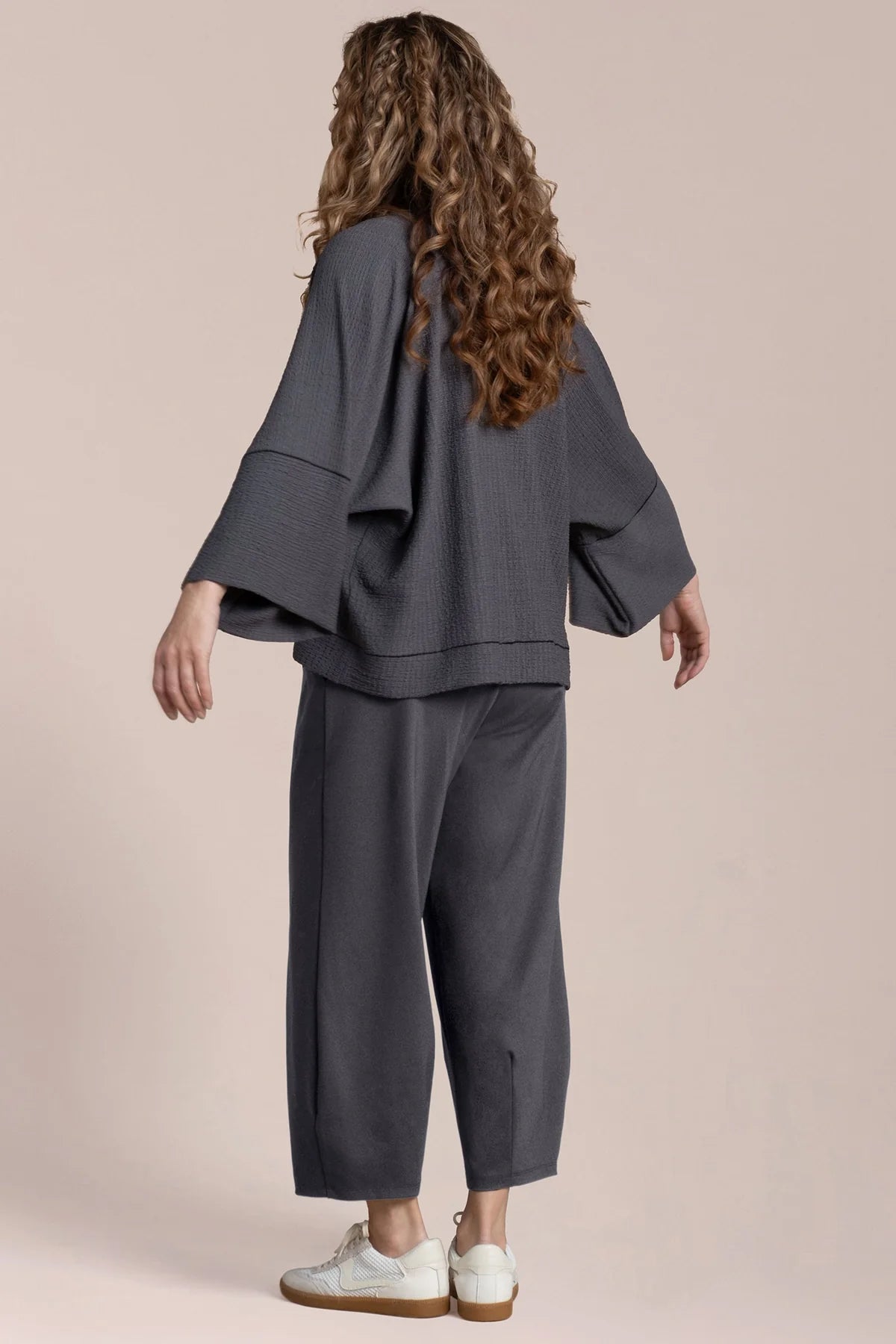 Person wearing a gray outfit with white shoes on a beige background