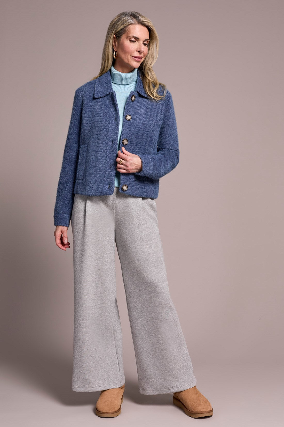 Woman wearing a blue jacket and gray pants on a beige background