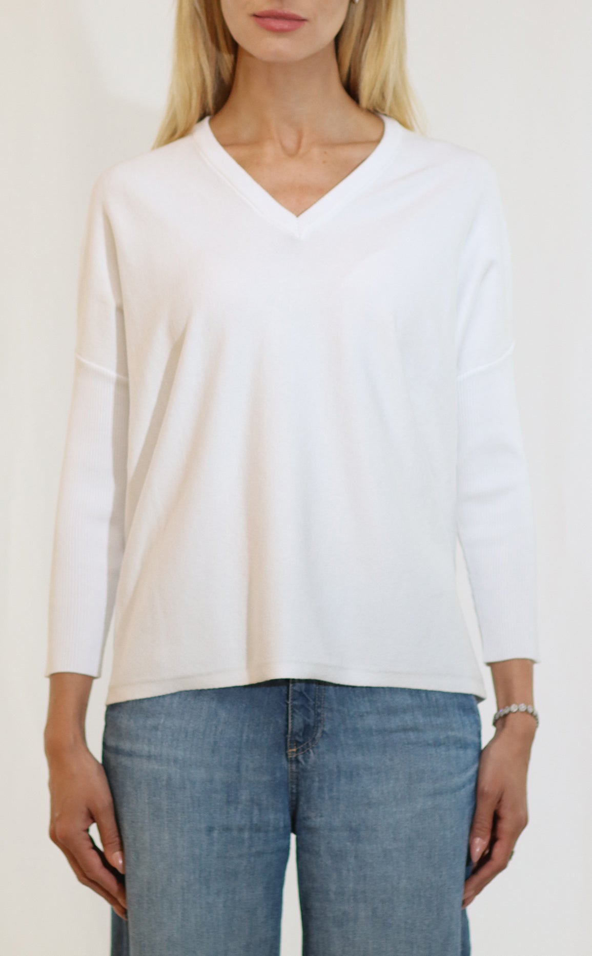 Person wearing a white long-sleeve top and blue jeans against a plain background