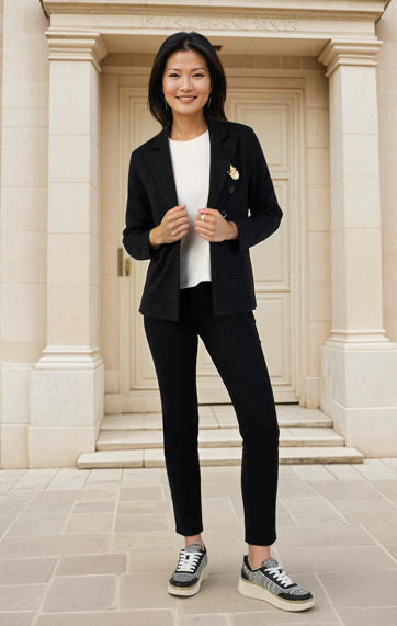 Woman in a black blazer and pants standing in front of a classical building entrance.