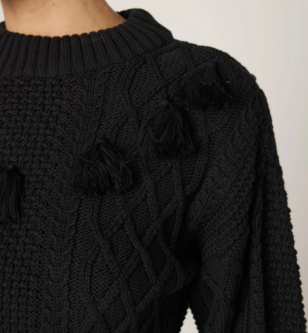 woman wearing a black knit sweater, textured with tassel details around the top