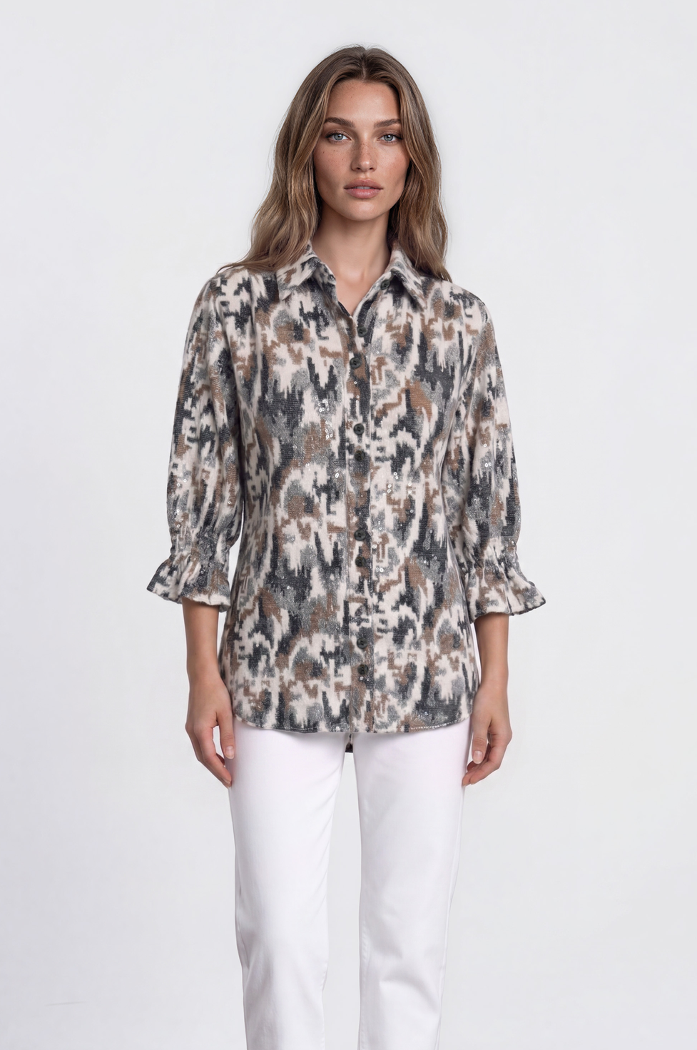 A woman stands in a studio wearing a long-sleeve button-up shirt with a beige, brown, and gray abstract pattern