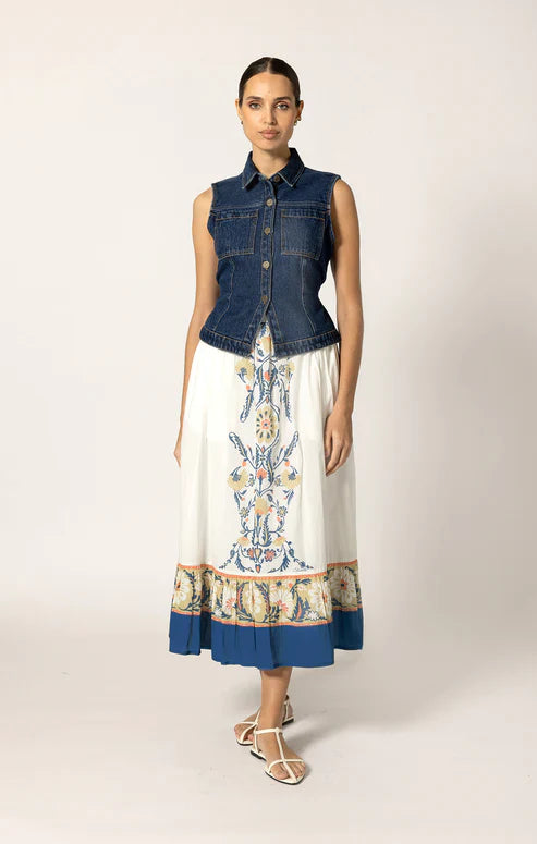 Woman wearing a denim vest over a patterned dress on a plain background