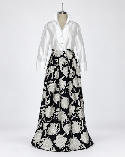 Connie Roberson Greyson Amazon Wrap Skirt A long formal dress displayed on a mannequin against a light gray studio background. The dress has a white satin long-sleeve button-front bodice and a full black skirt with large silver floral embroidery.