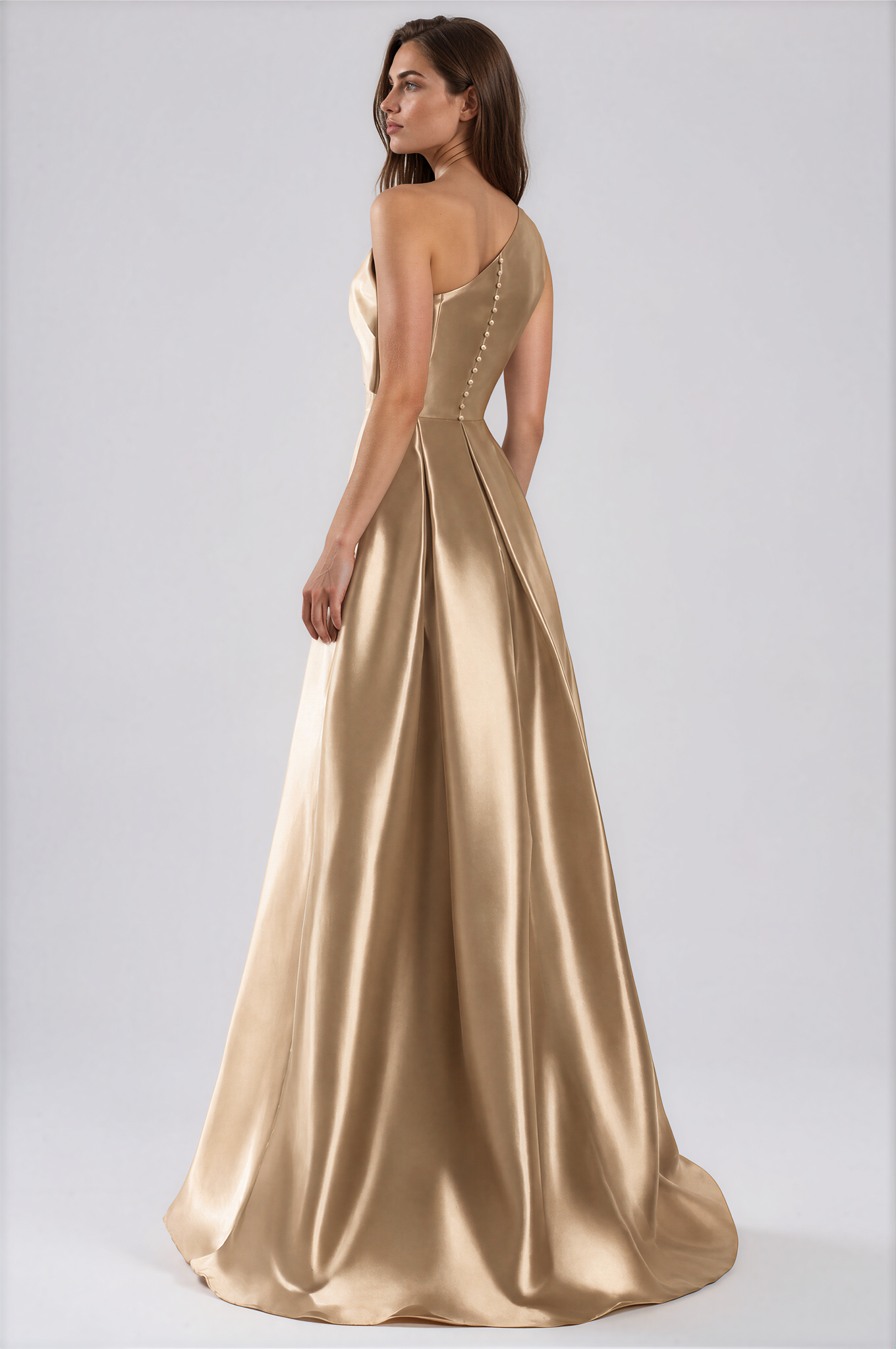 A woman modeling a floor-length satin gown in a warm champagne-gold tone by Daymor One-Shoulder Bow Organza Gown