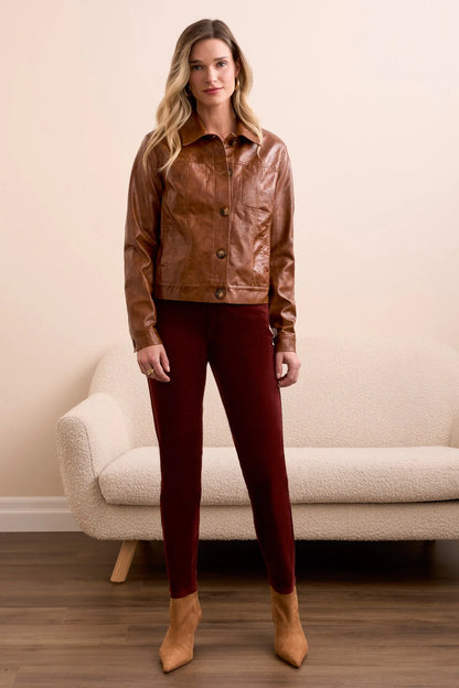 Woman wearing a brown leather jacket and red pants standing in a room with a beige couch.