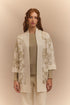 Woman wearing a stylish beige cardigan with floral patterns on a beige background