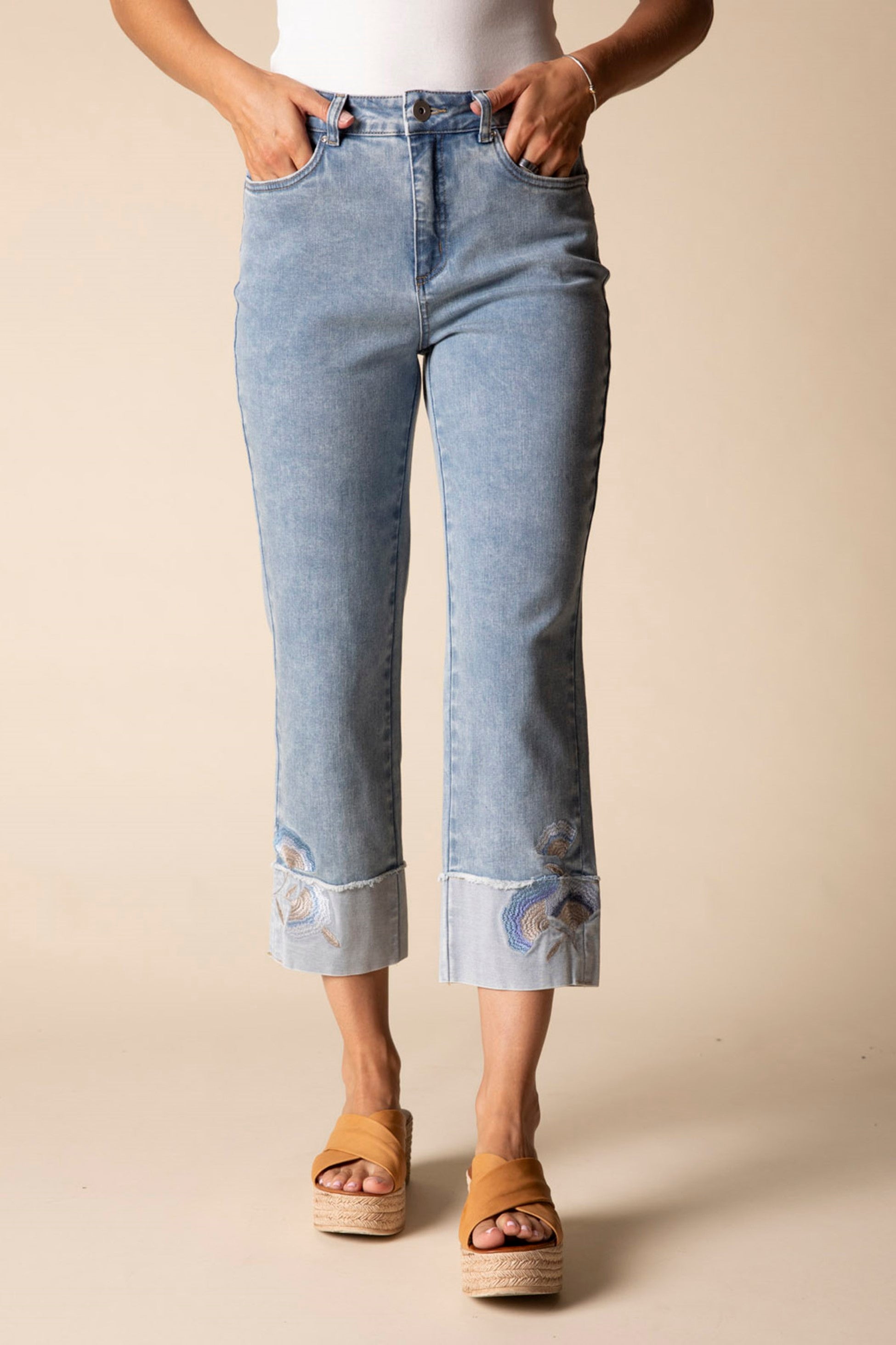 Person wearing light blue jeans with rolled-up cuffs on a beige background