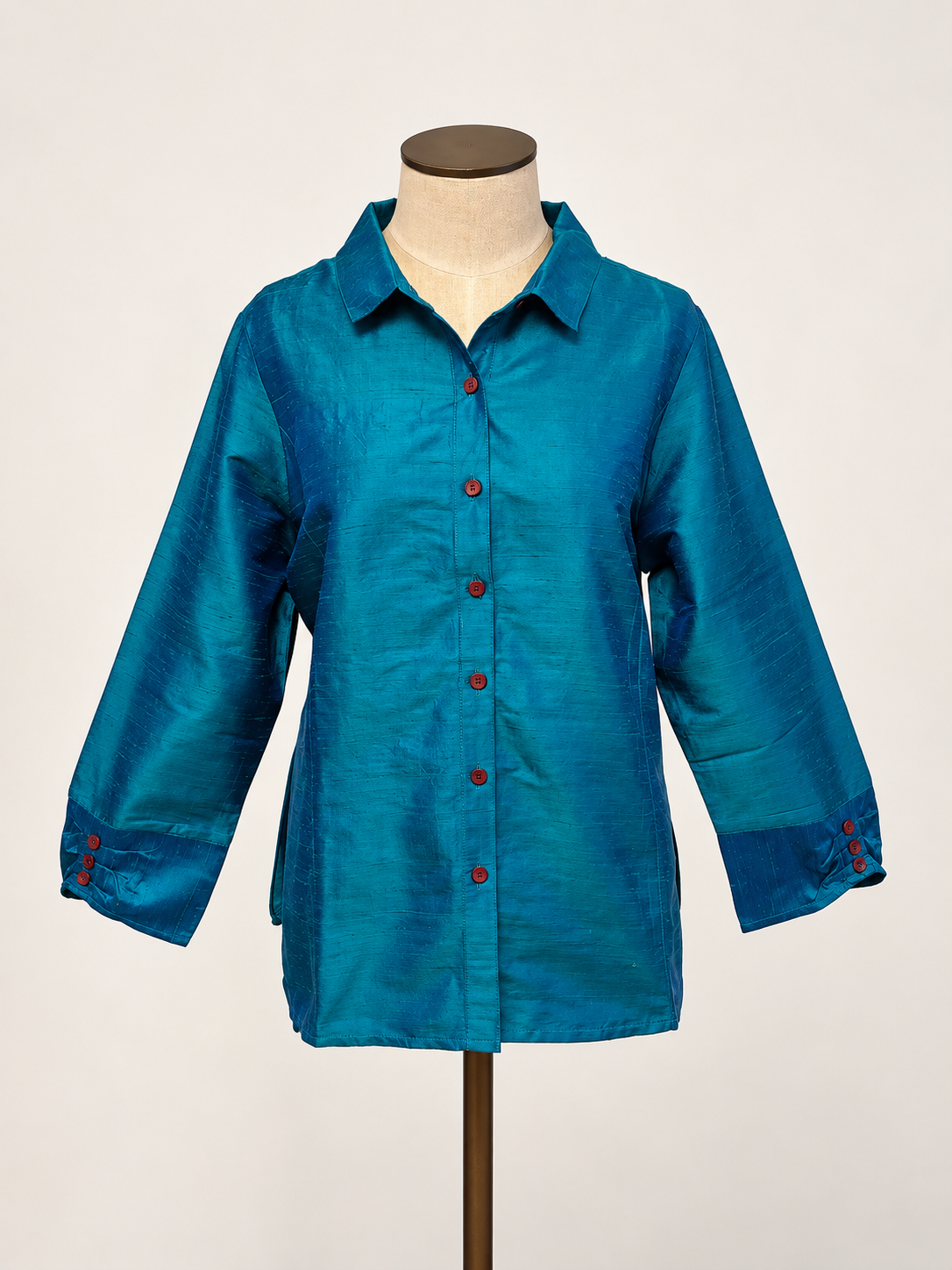 A teal blue silk long-sleeve button-up shirt with red buttons