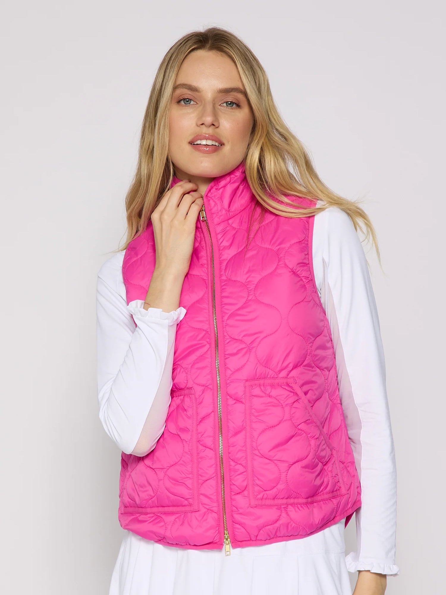 Woman wearing a bright pink quilted vest over a white shirt on a light gray background