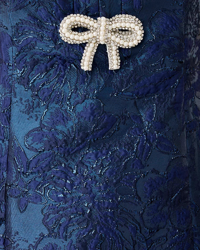 Close-up of a blue floral lace fabric with a decorative bow brooch.