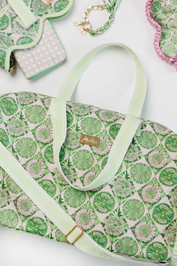 A Lilly Pulitzer Duffle Tote, Tropical Tiles tote bag with a green and pink citrus slice pattern, featuring pale green handles and a small gold-tone Lilly Pulitzer logo plaque. 