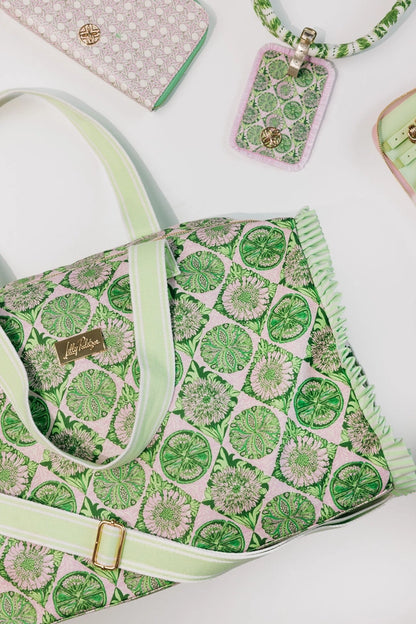 A Lilly Pulitzer Duffle Tote, Tropical Tiles tote bag with a green and pink citrus slice pattern, featuring pale green handles and a small gold-tone Lilly Pulitzer logo plaque. 