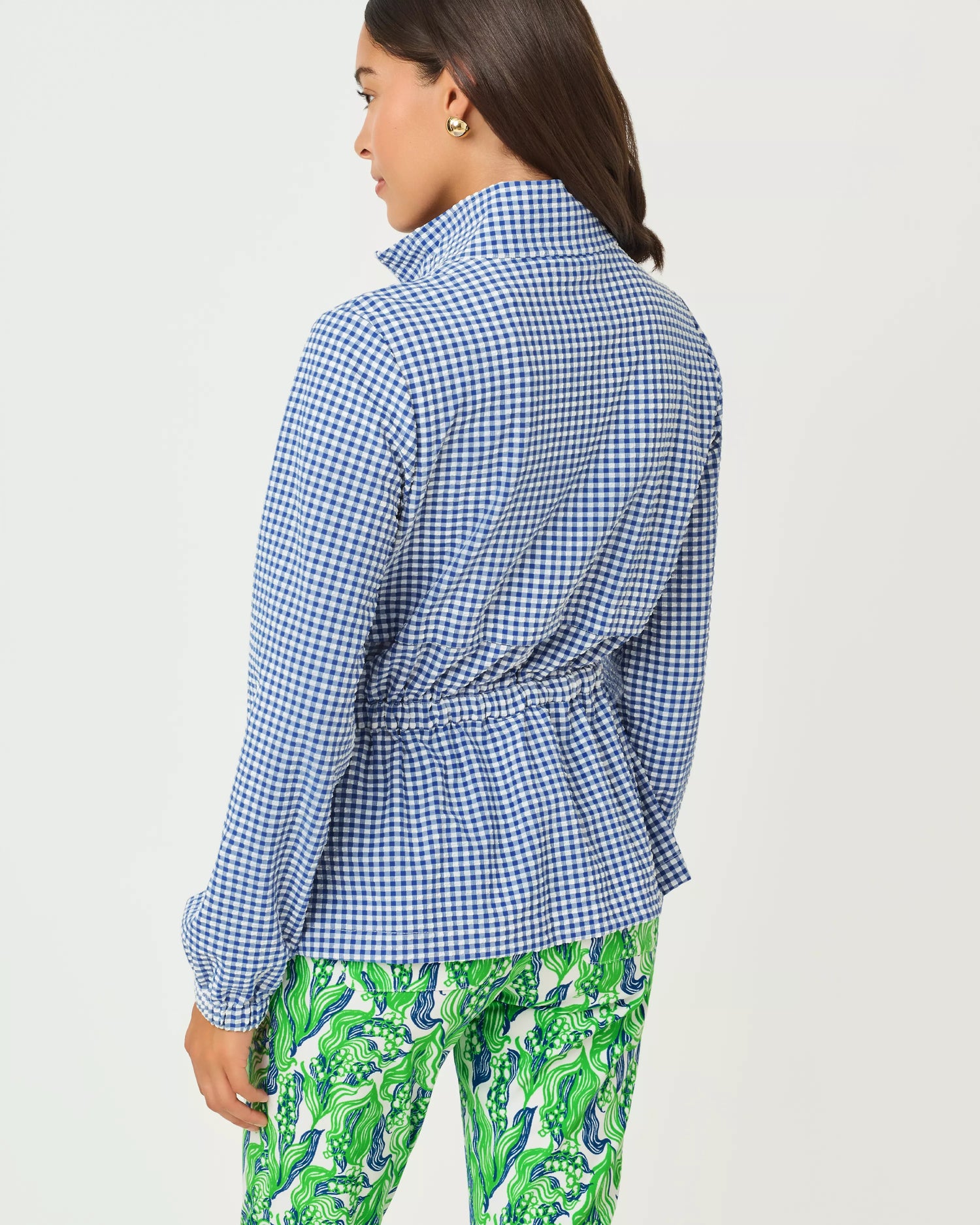 Woman wearing a blue checkered shirt and green patterned pants on a white background