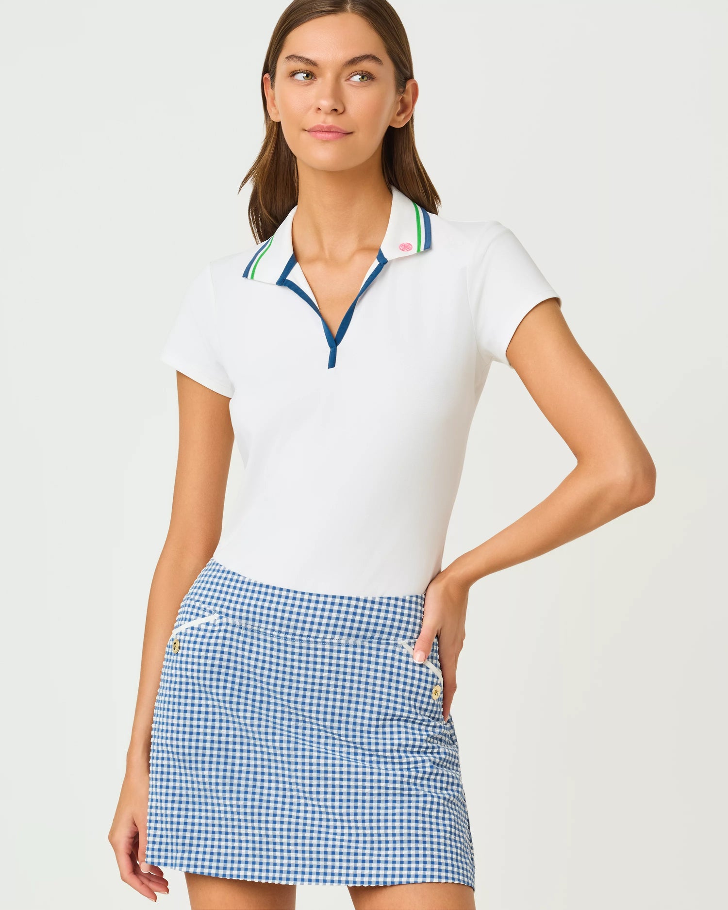 Woman wearing a white polo shirt with colorful trim and a blue checkered skirt on a light gray background