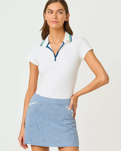 Woman wearing a white polo shirt with colorful trim and a blue checkered skirt on a light gray background