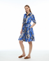 A woman modeling a blue knee-length dress with a black and white floral print, featuring a tie-neck detail and a matching waist tie Patty Kim Kelly Dress Blue Chocolate Color
