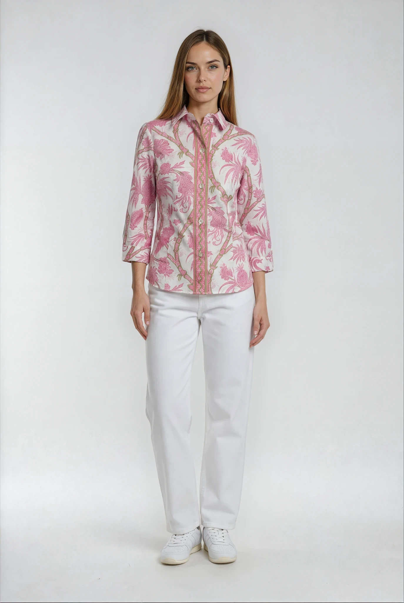 Woman wearing a pink floral blouse and white pants on a white background
