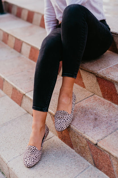 Person wearing black pants and leopard print shoes sitting on stone steps.