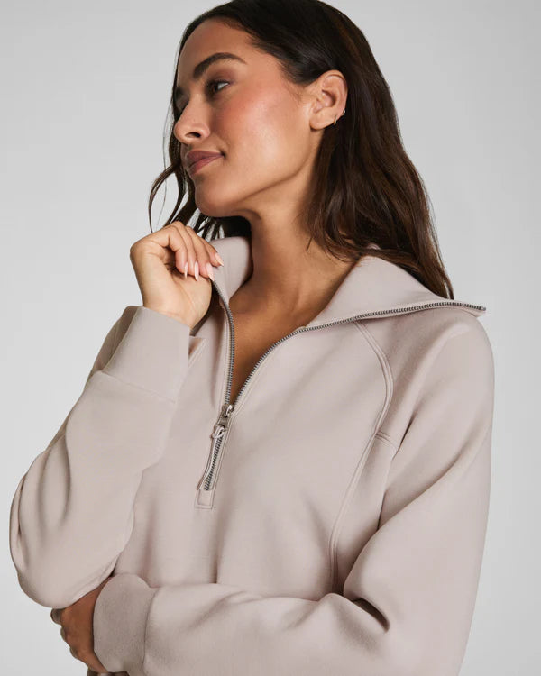 Woman wearing a beige zip-up hoodie against a plain background