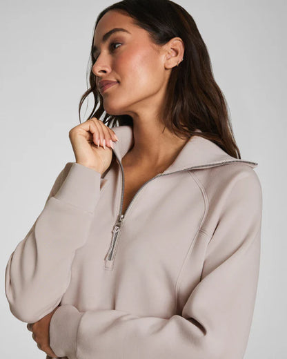Woman wearing a beige zip-up hoodie against a plain background