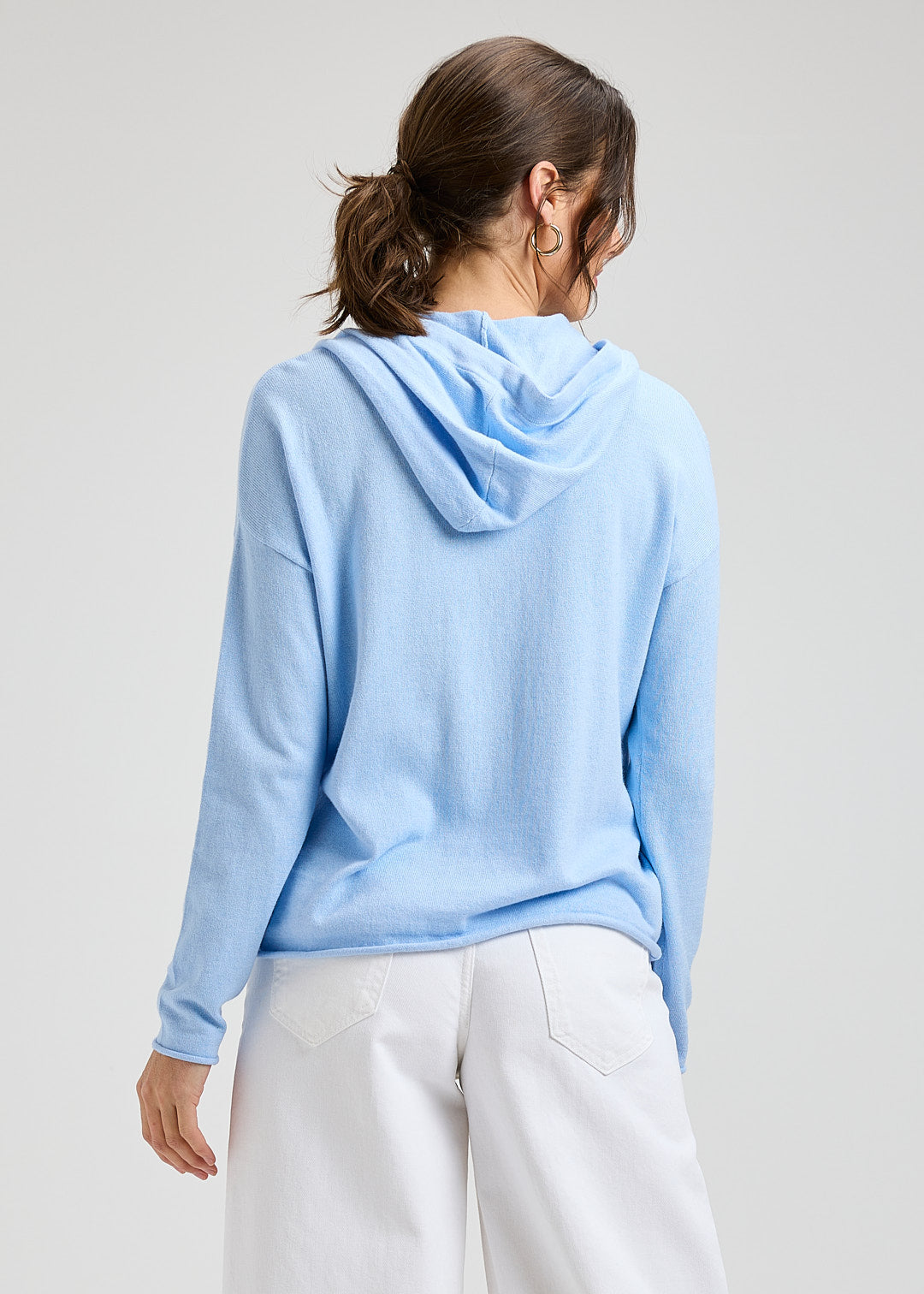 Person wearing a light blue hoodie and white pants on a plain background