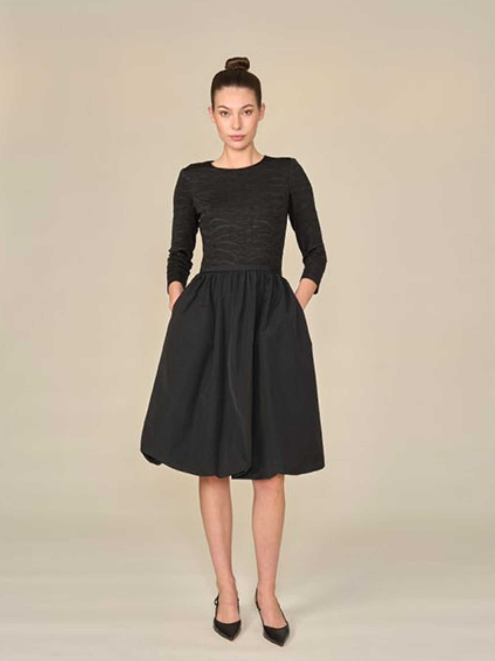 Woman wearing a black dress against a beige background.