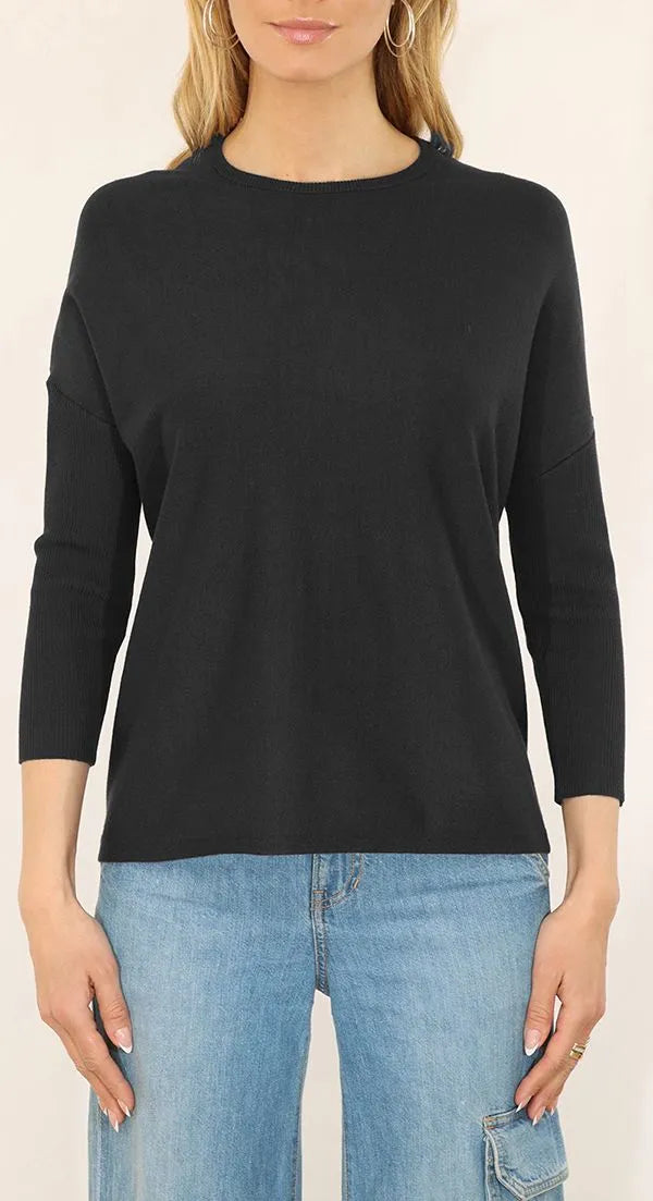 Person wearing a black long-sleeve top and blue jeans on a beige background